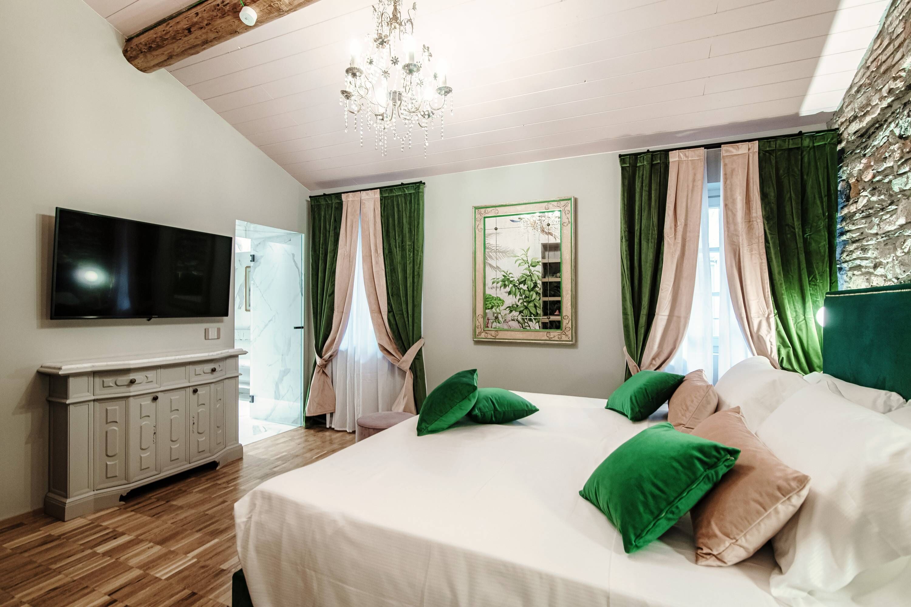 A bedroom with a large bed, a TV, a wooden cabinet, and a chandelier.