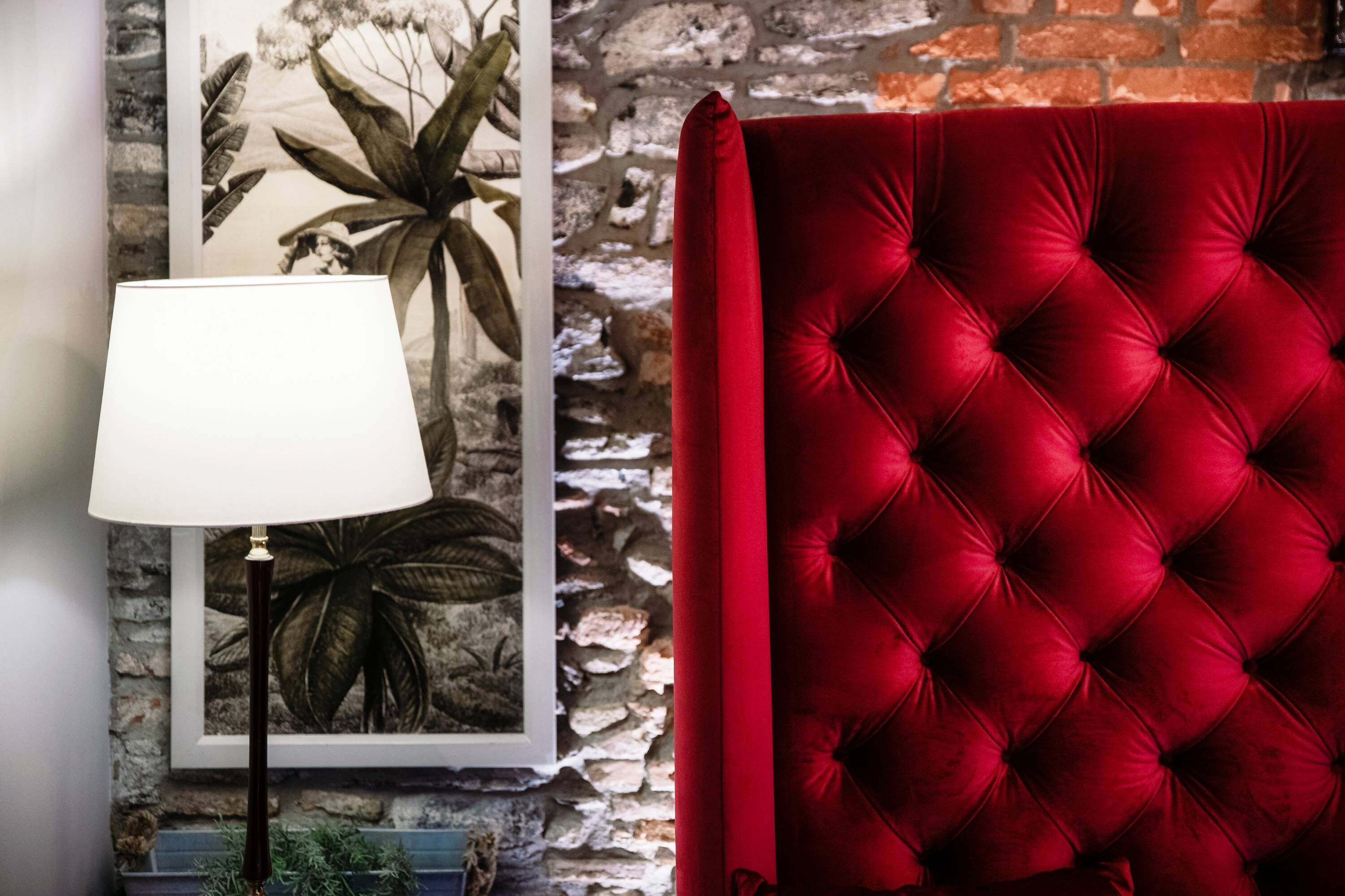 A room with a red upholstered headboard, a framed botanical print on the wall, and a floor lamp.