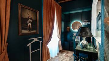 A room with a wooden floor, a table with a lamp, a framed picture on the wall, and a window with curtains.