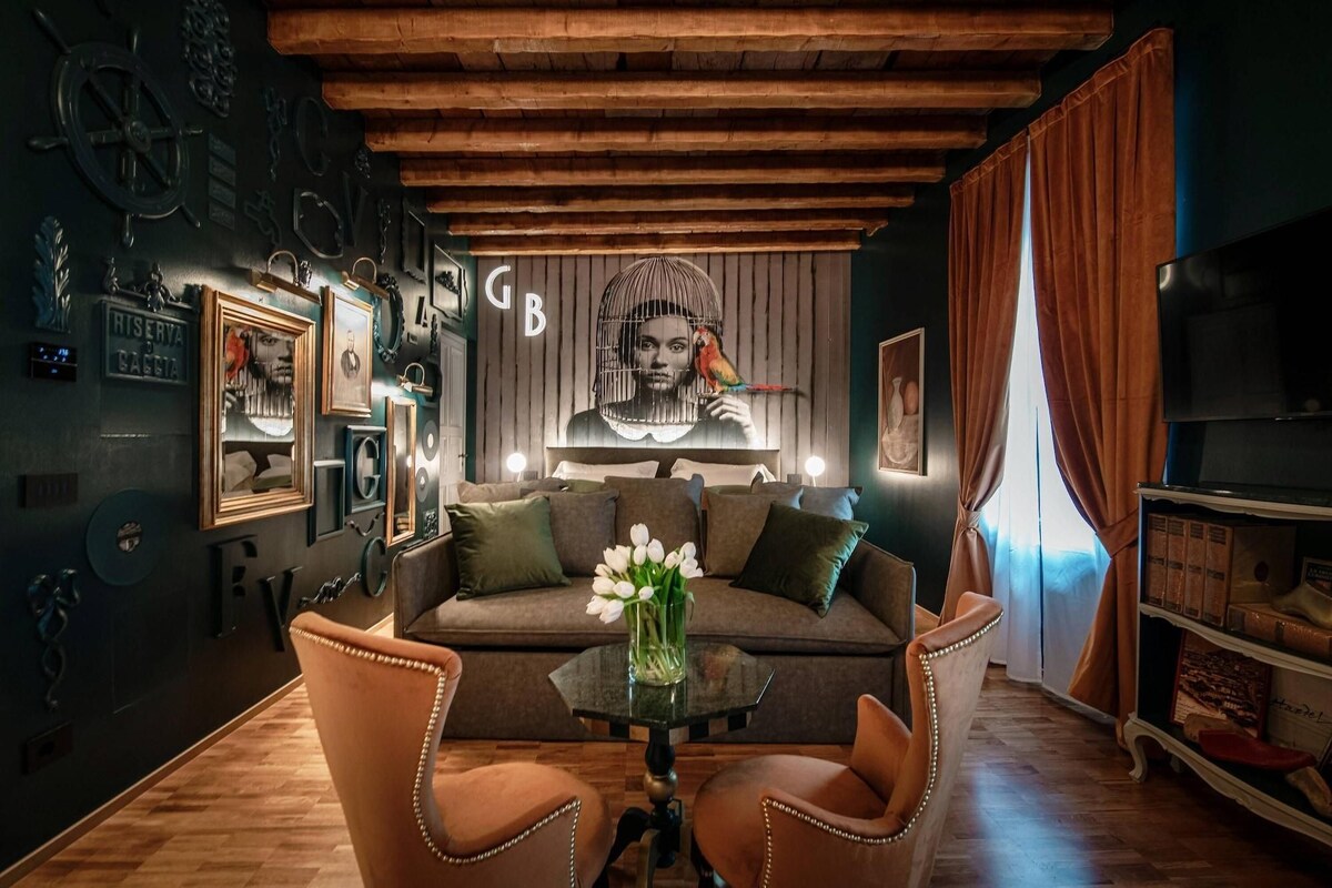 A cozy living room with a wooden ceiling, a sofa, two armchairs, a coffee table with flowers, and a television.