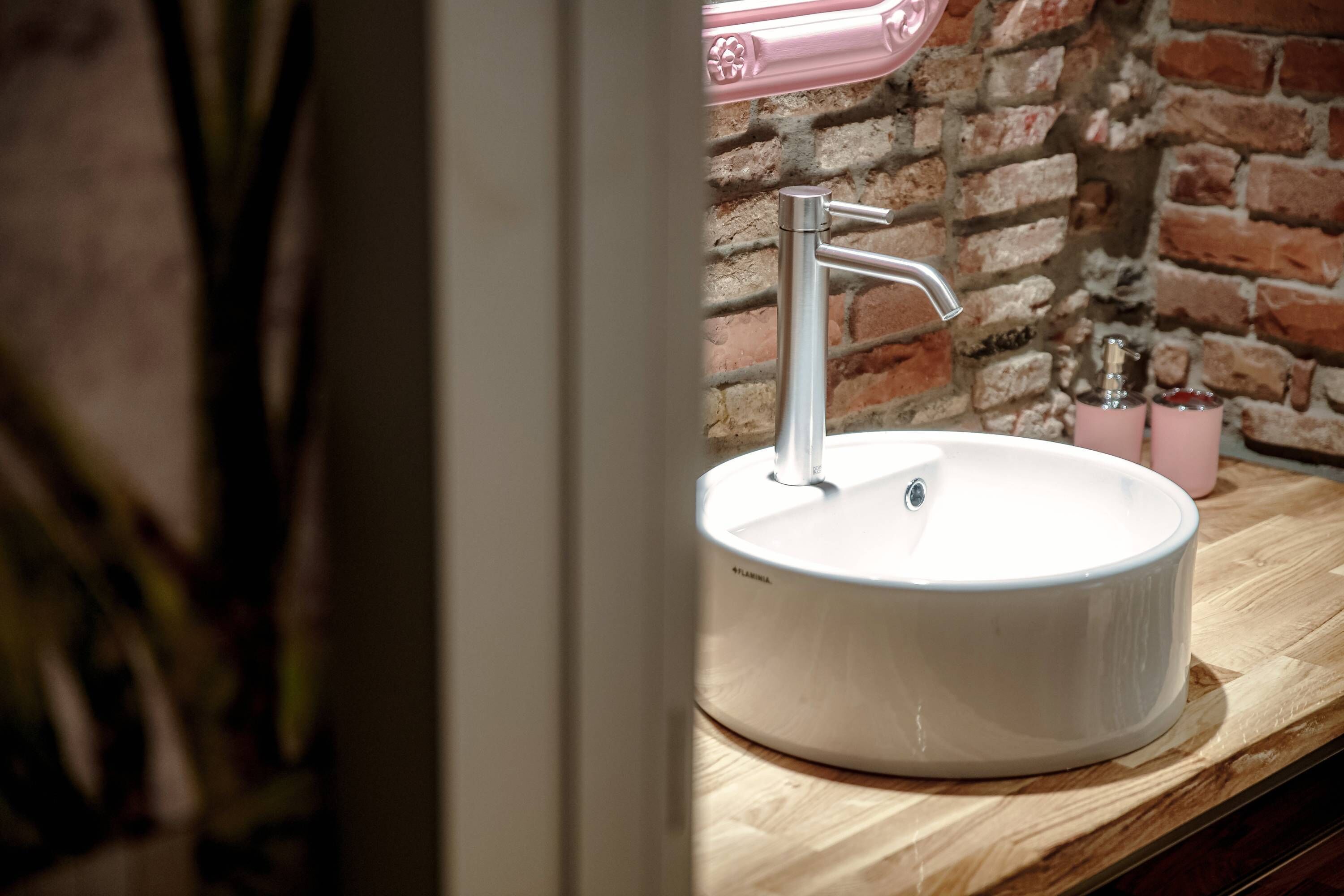 Une salle de bain avec un lavabo blanc, un robinet moderne et un mur en briques.