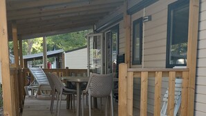 Ein überdachter Außenbereich mit Holzdeck, einem Tisch mit Stühlen und einer kleinen Veranda mit Geländer.