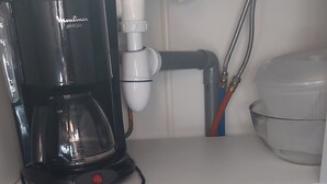 Eine Küchenzeile mit einer Kaffeemaschine, einem Sieb und einer Pfanne auf einem weißen Regal.