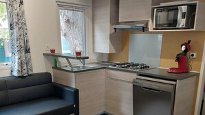 Eine kompakte Küche mit Gasherd, Mikrowelle und Kaffeemaschine. Im Wohnbereich befindet sich eine Couch und ein kleiner runder Tisch.