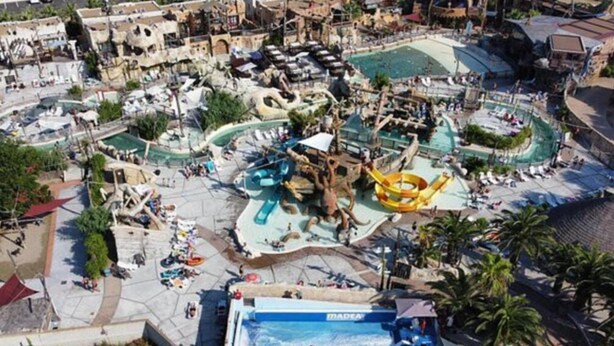 Ein Luftbild eines Wasserparks mit mehreren Wasserrutschen und Pools, umgeben von Gebäuden und Palmen.