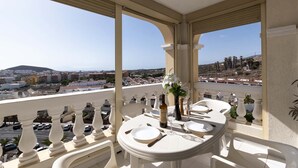 Een balkon met een eettafel, met uitzicht op een stadsgezicht met gebouwen en palmbomen.