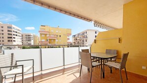 Un balcón con una mesa y sillas, una pared amarilla y vistas de edificios circundantes.