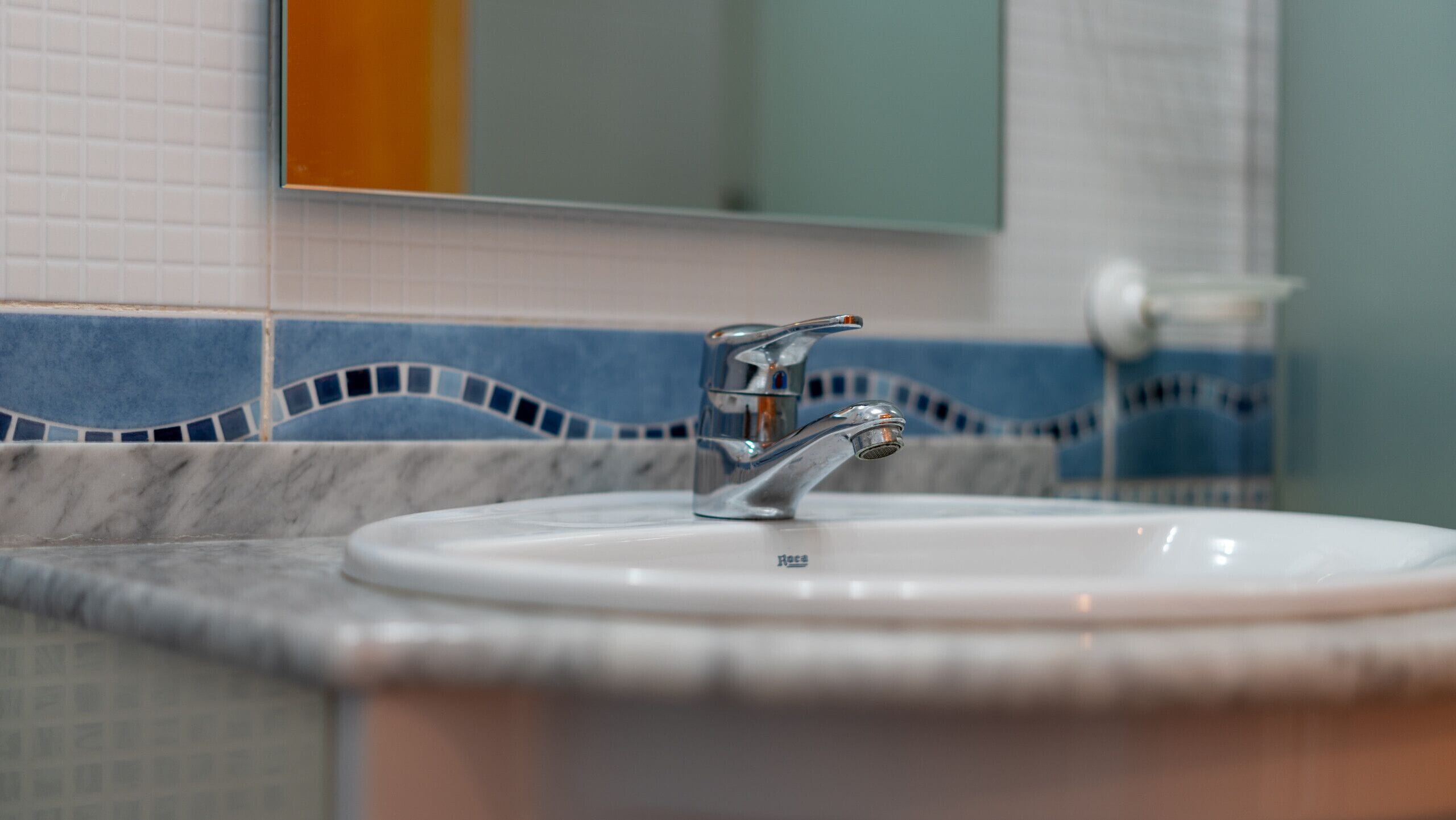 Un lavabo de baño con un grifo moderno, un espejo encima y paredes con azulejos azules y blancos.