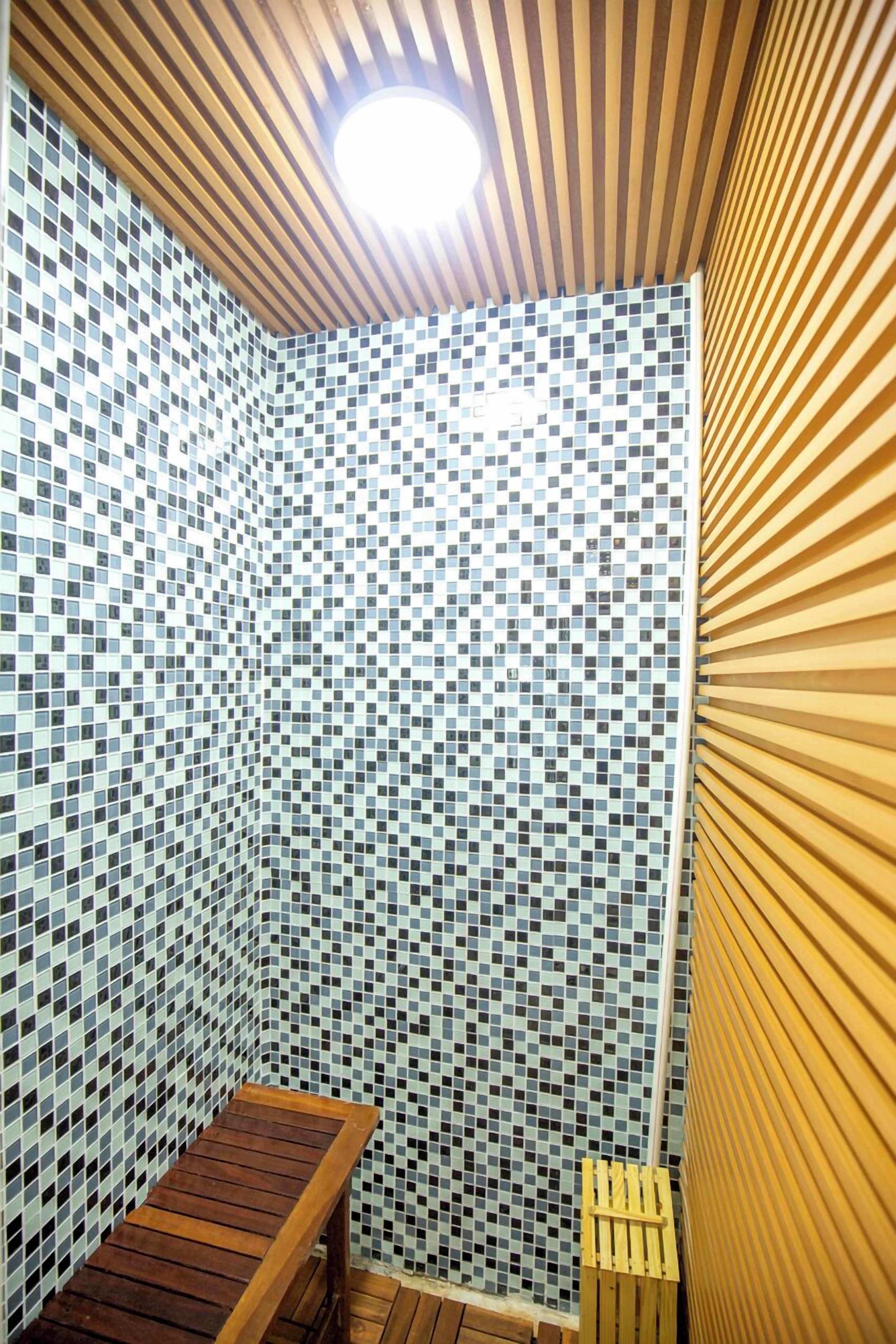 Un petit espace clos, avec un mur décoré d’une mosaïque de carreaux, un banc en bois et un mur en bois à lattes sur l’un des côtés.