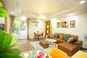 A modern living room with a brown leather sofa, a dining table with chairs, a small coffee table, and a large window with curtains.
