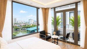 Moderni hotellihuone, jossa on suuri sänky, tuoleilla varustettu parveke ja näkymä kaupunkiin.