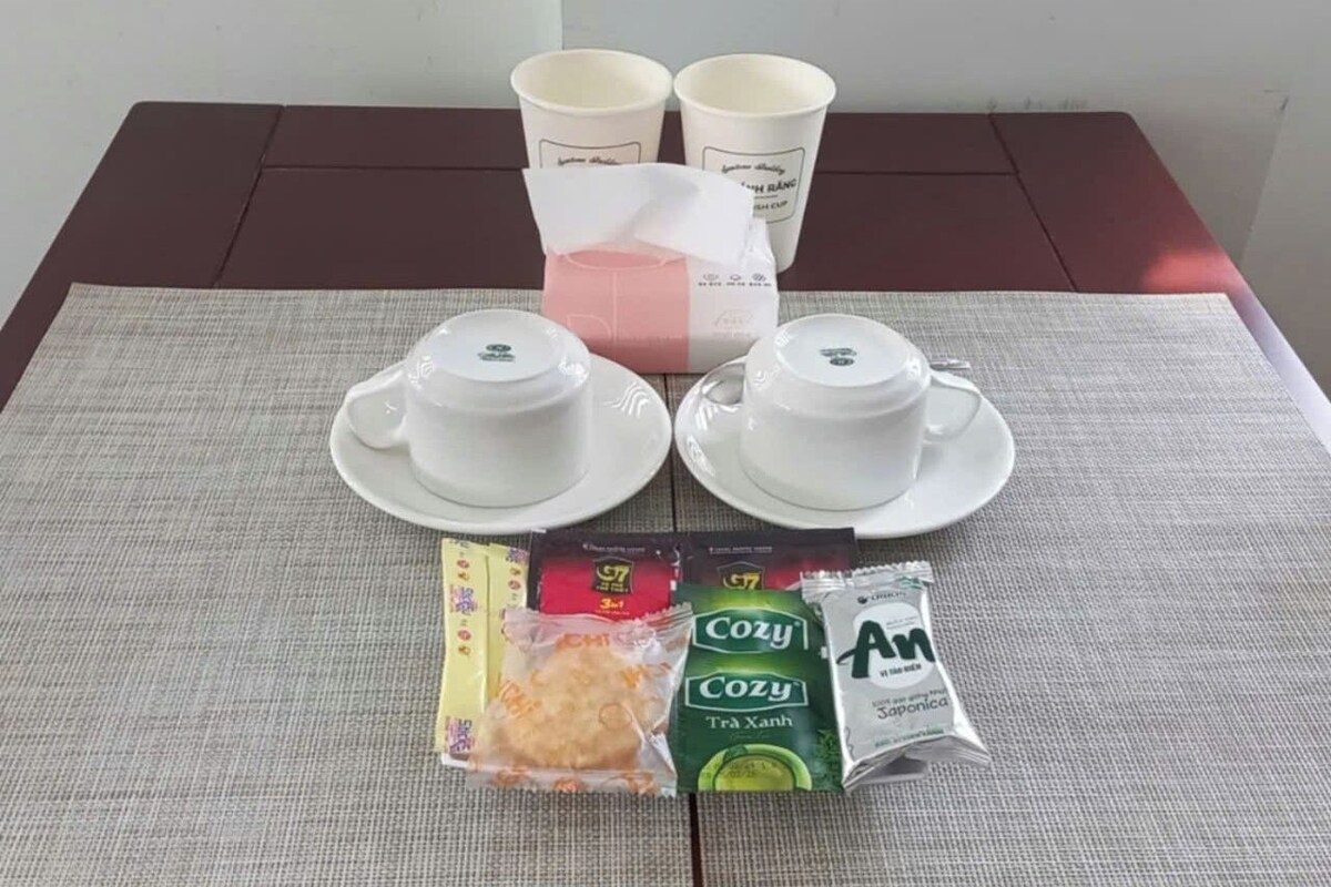 Una mesa con dos tazas y platillos blancos, una caja de pañuelos rosa, y paquetes de aperitivos y té.