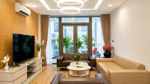 A modern living room with a flat-screen TV, leather sofas, a coffee table, and a large window with a view of palm trees.