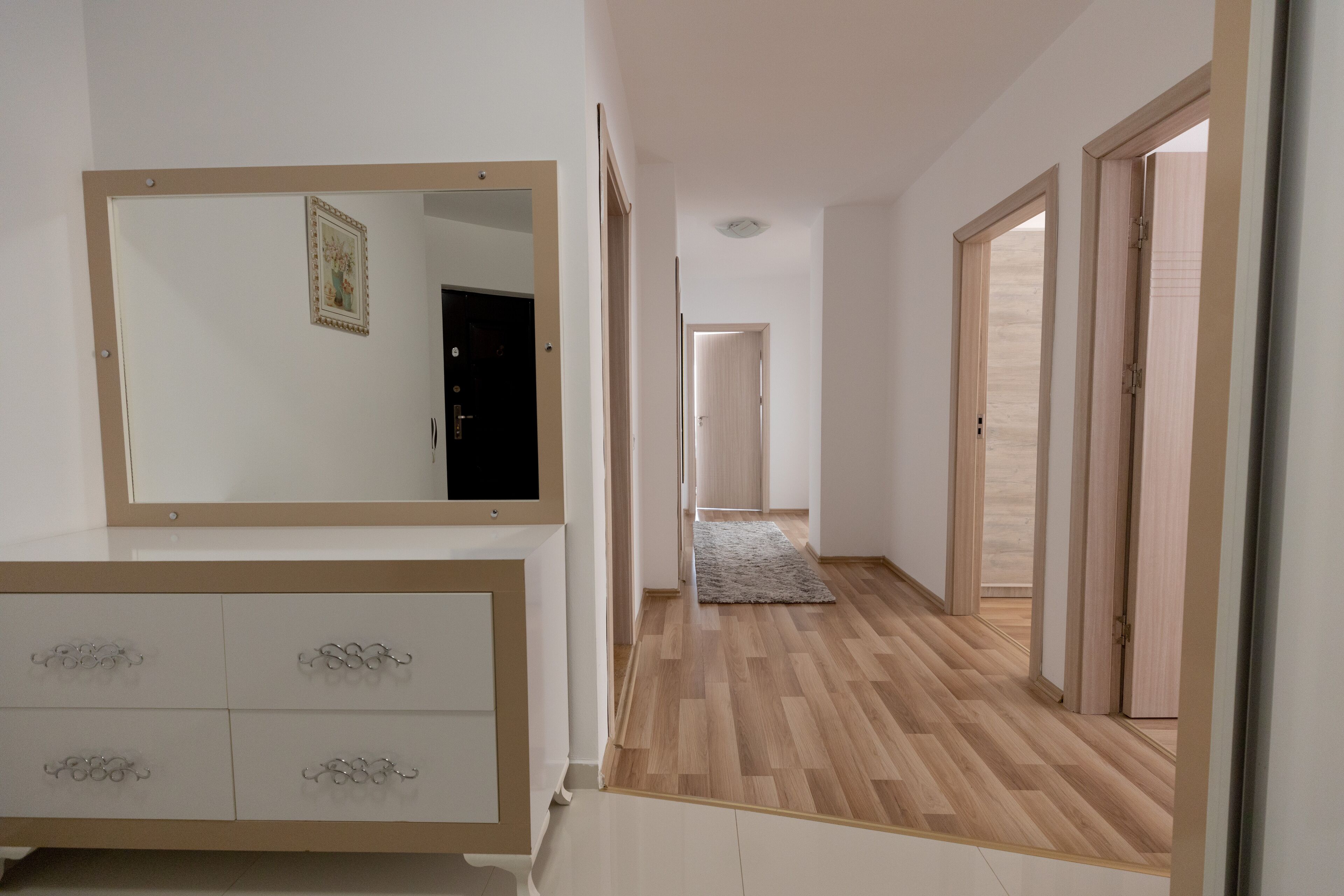 A hallway with a wooden floor, a white dresser with drawers, and a mirror.