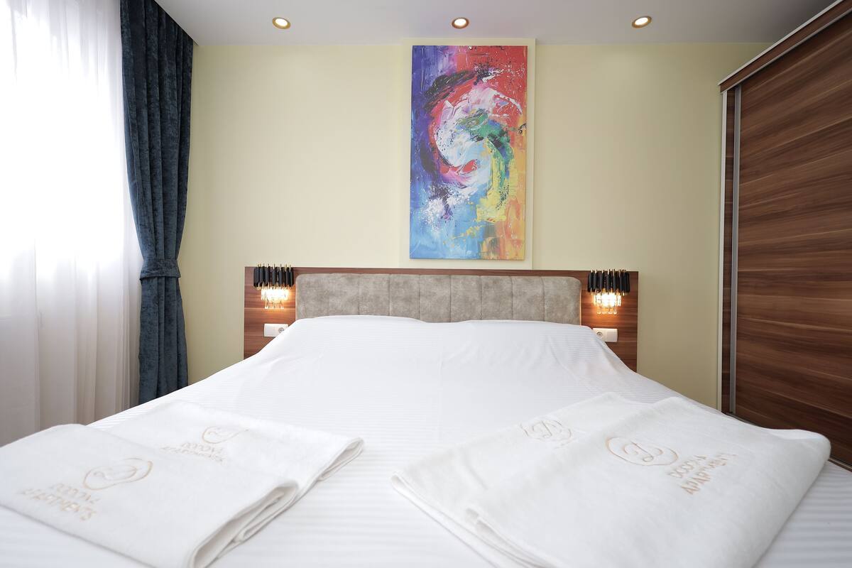 Ein Hotelzimmer mit einem großen Bett, zwei Nachttischlampen, einem farbenfrohen abstrakten Gemälde an der Wand und einem Holzkopfende.