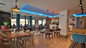 Un restaurante espacioso con mesas y sillas de madera, lámparas colgantes azules y rojas, y un diseño de techo moderno.