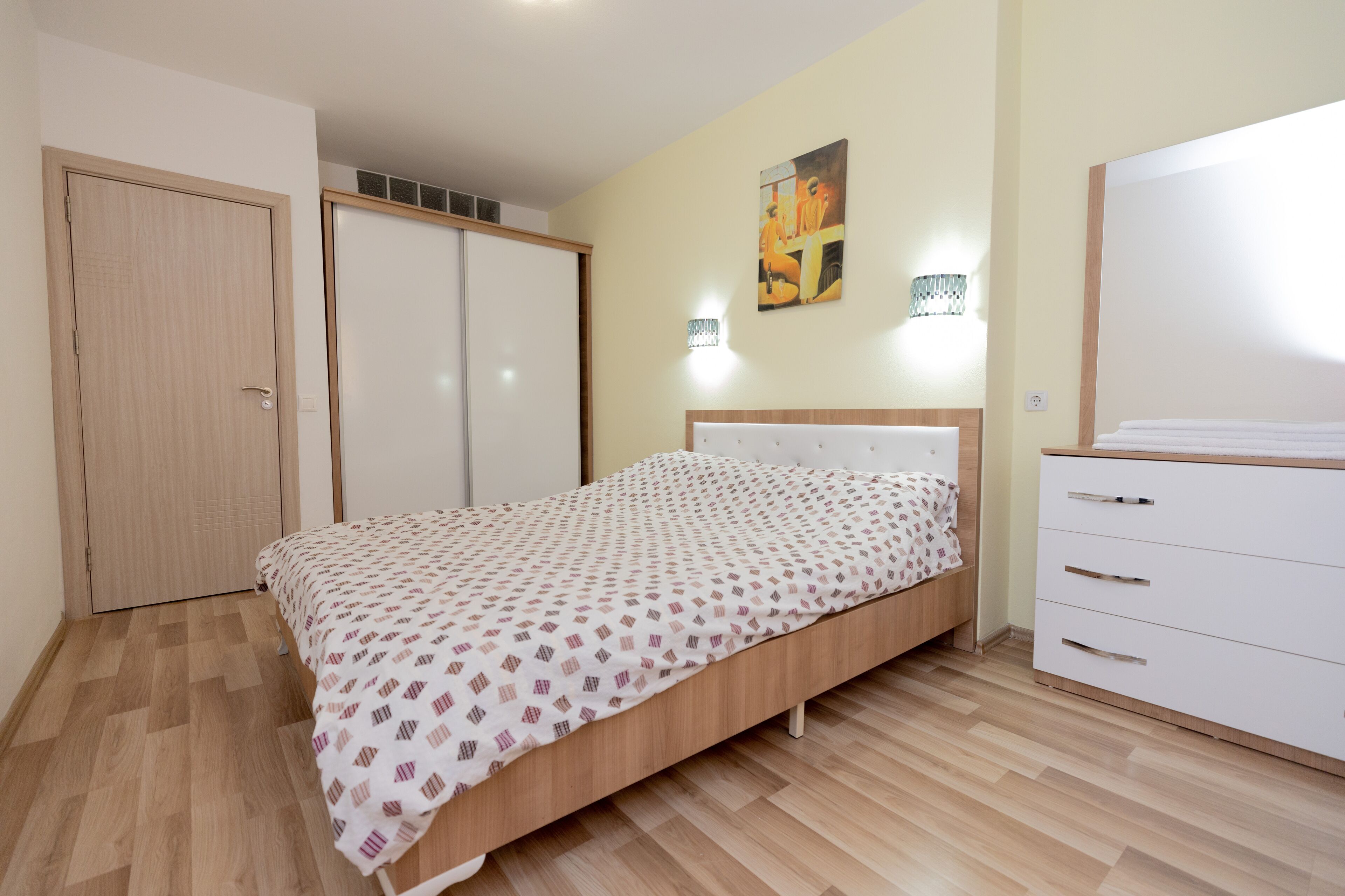 A bedroom with a bed, a wardrobe, a desk, and a painting on the wall.
