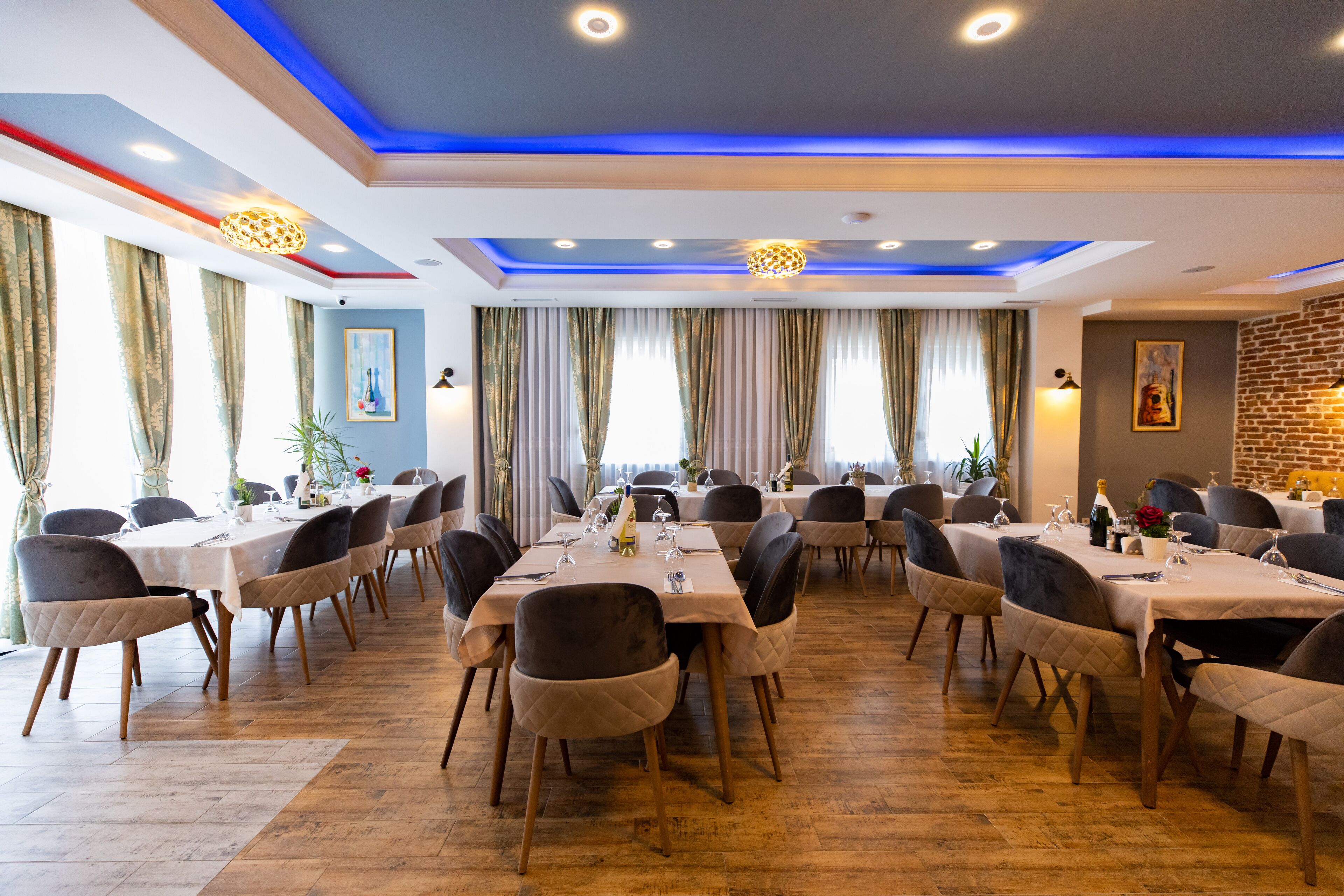 Un comedor con varias mesas y sillas, pared de ladrillo e iluminación azul en el techo.