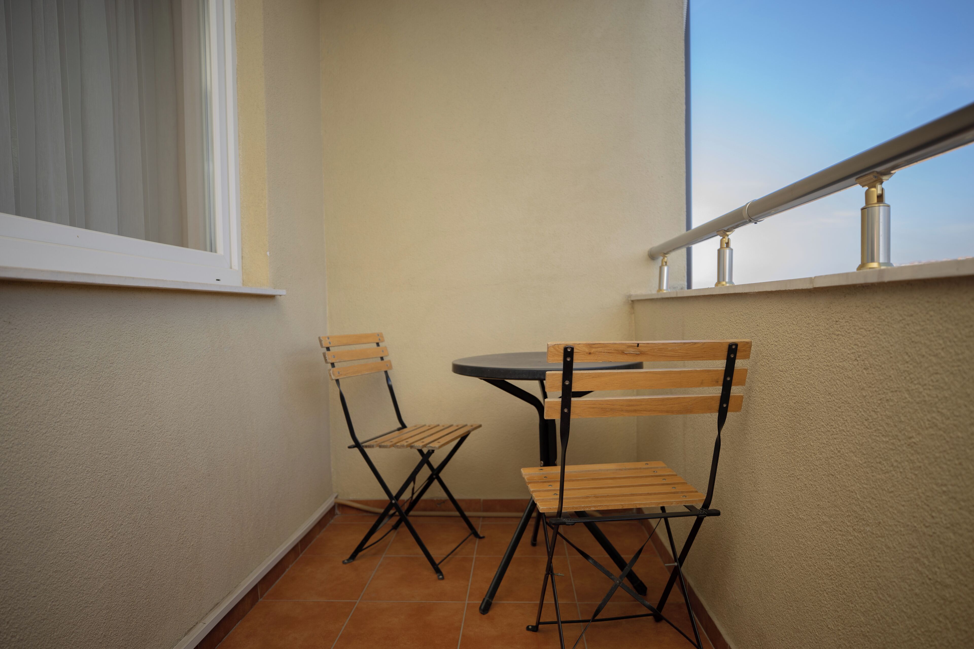 A small balcony with a table and two chairs, a window, and a railing.