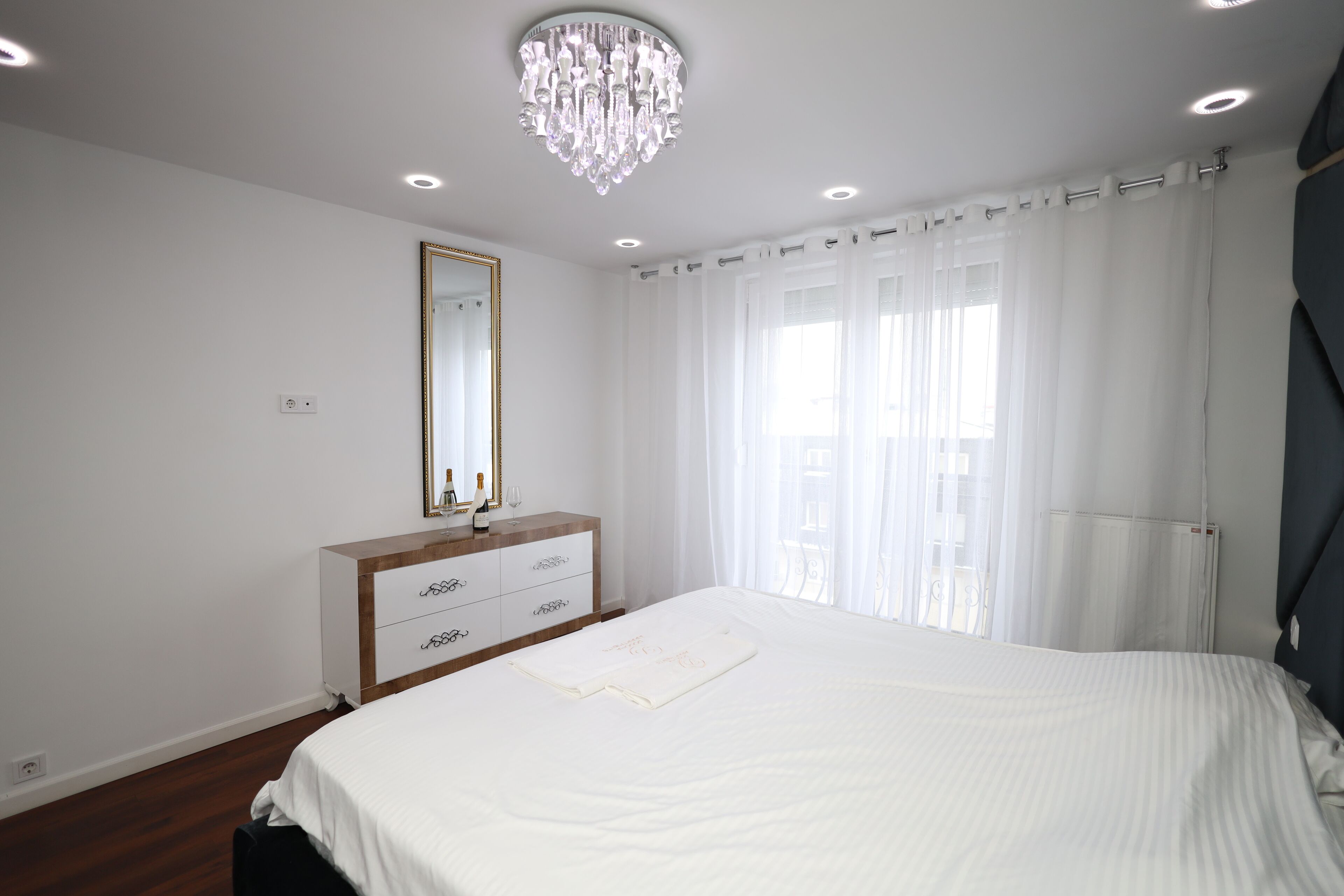 A bedroom with a large bed, a dresser, a mirror, and a chandelier.