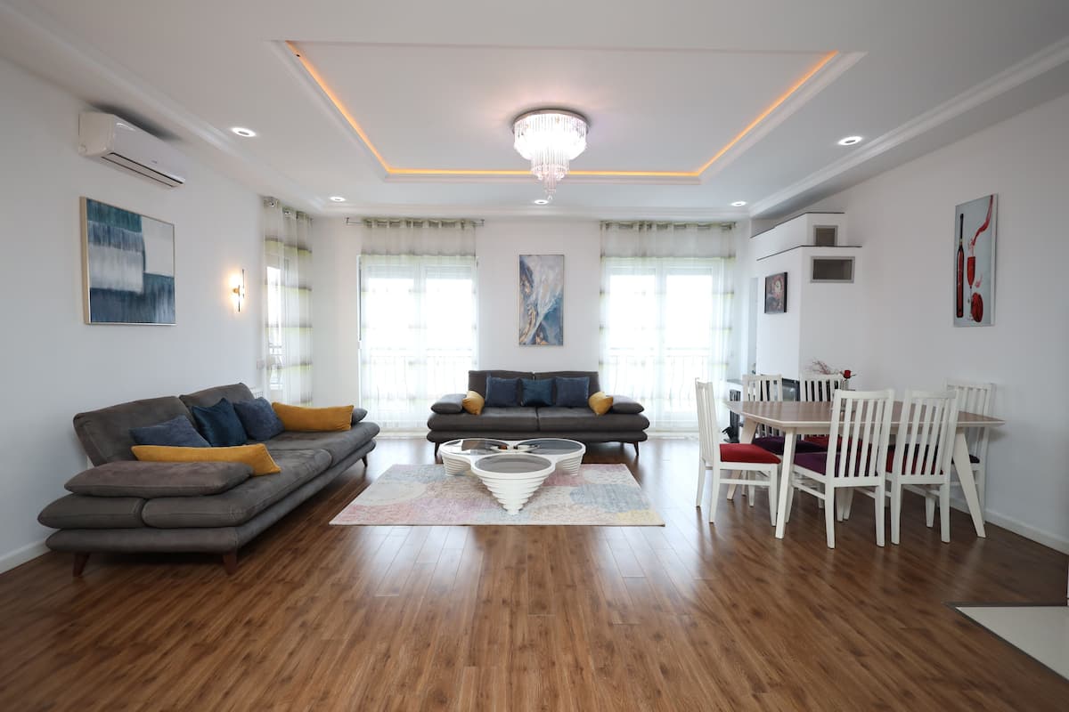Ein modernes Wohnzimmer mit einem grauen Ecksofa, einem weißen Couchtisch und einem Essbereich mit weißen Stühlen.