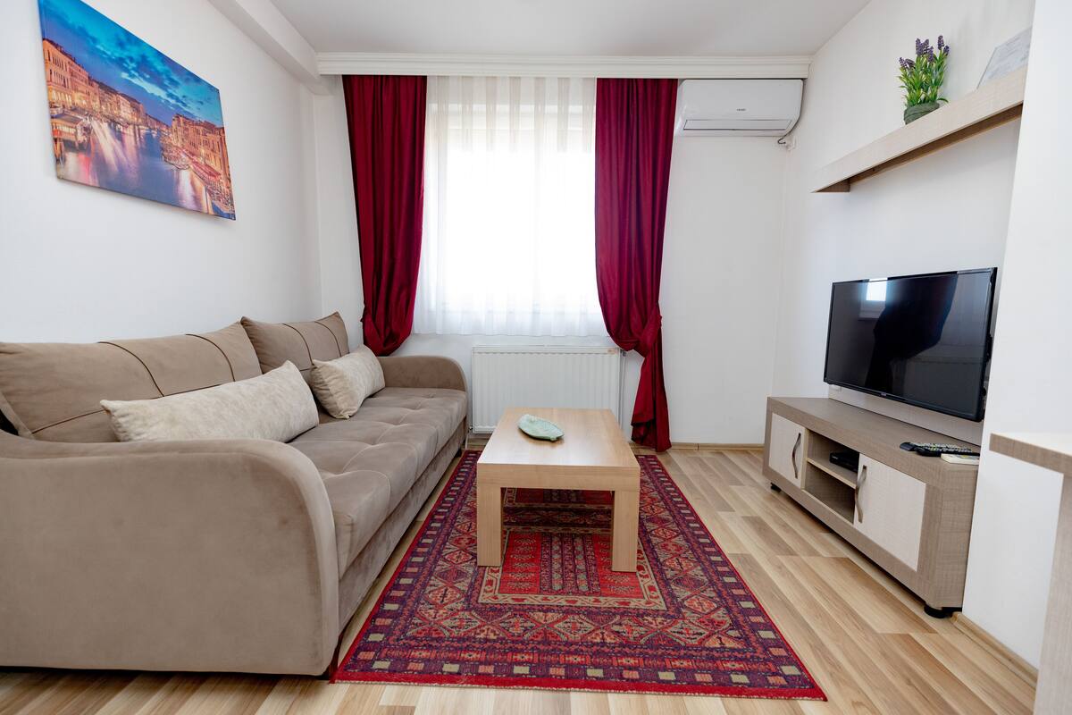 Ein Wohnzimmer mit Sofa, Couchtisch, Fernseher und einem gemusterten Teppich.
