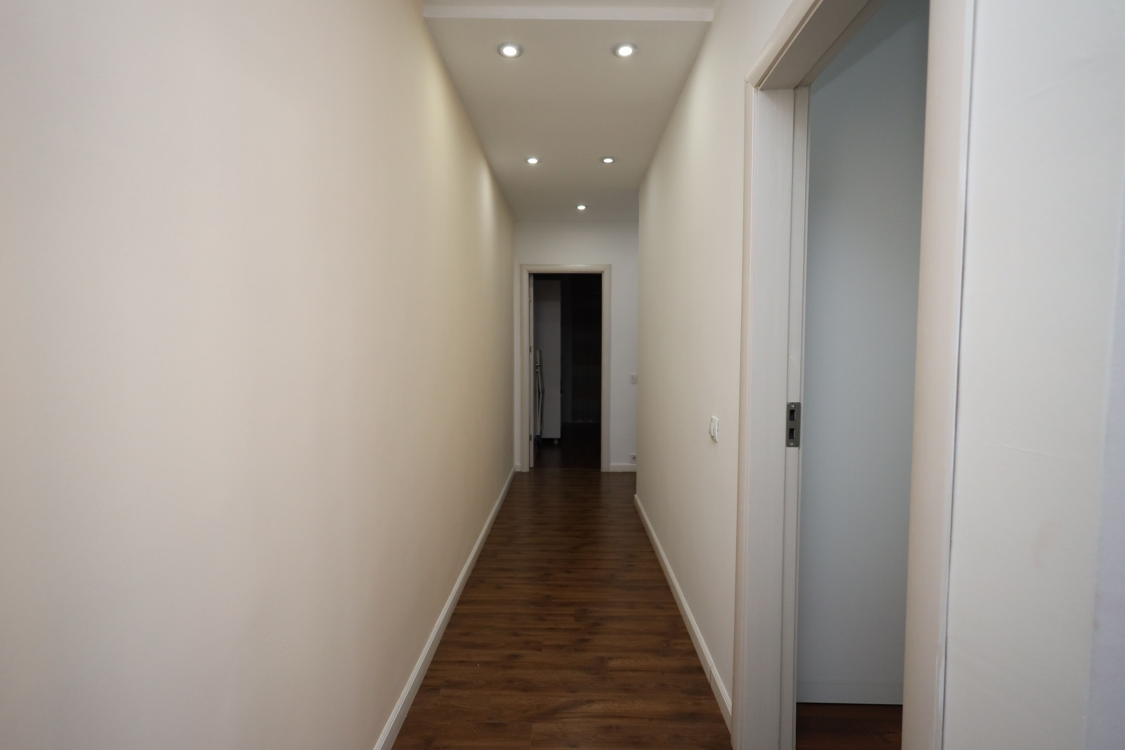 A narrow hallway with wooden flooring and white walls.