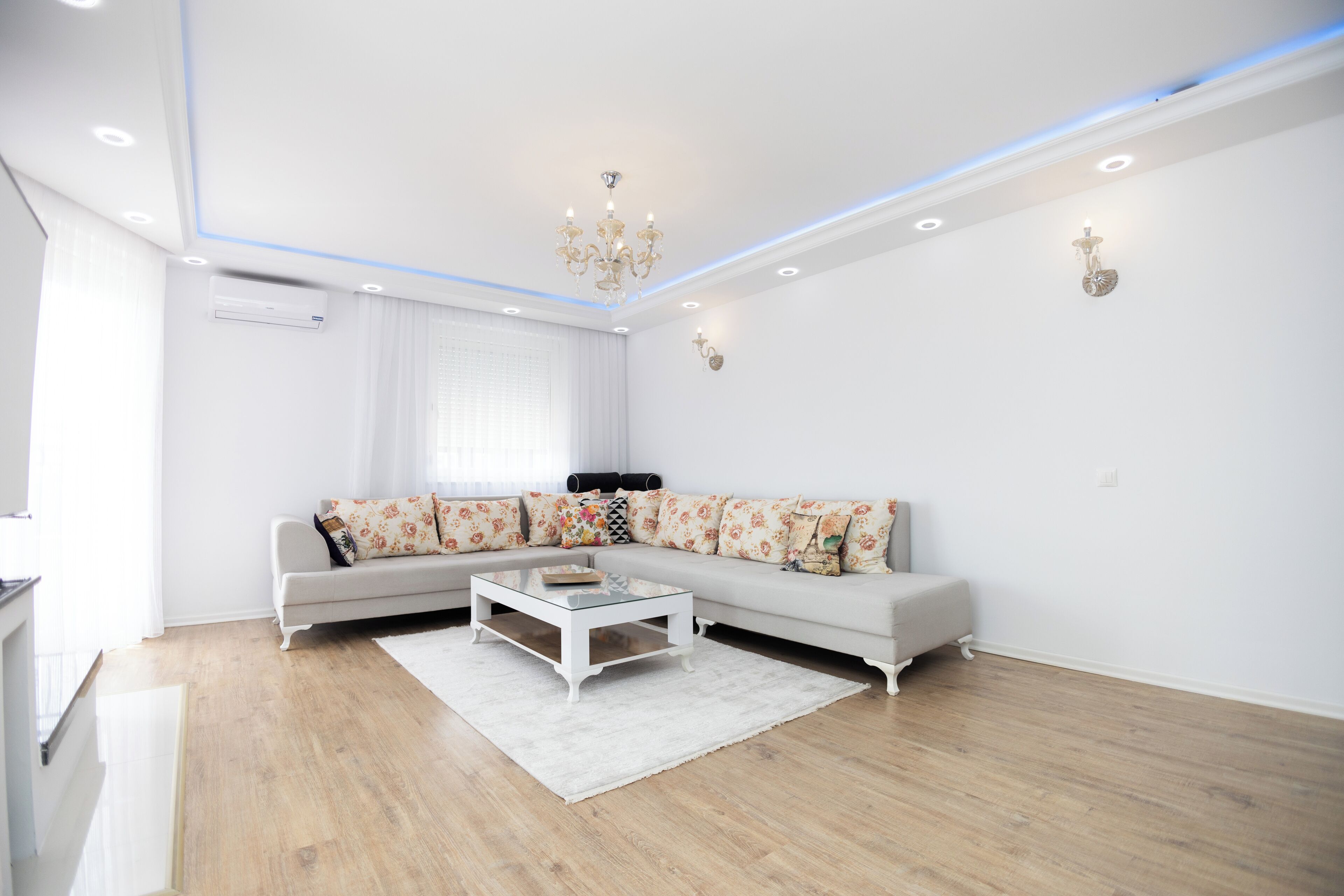 A modern living room with a sectional sofa, a glass coffee table, and a chandelier.