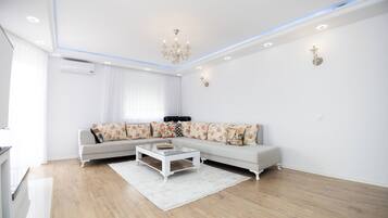 A modern living room with a sectional sofa, a glass coffee table, and a chandelier.