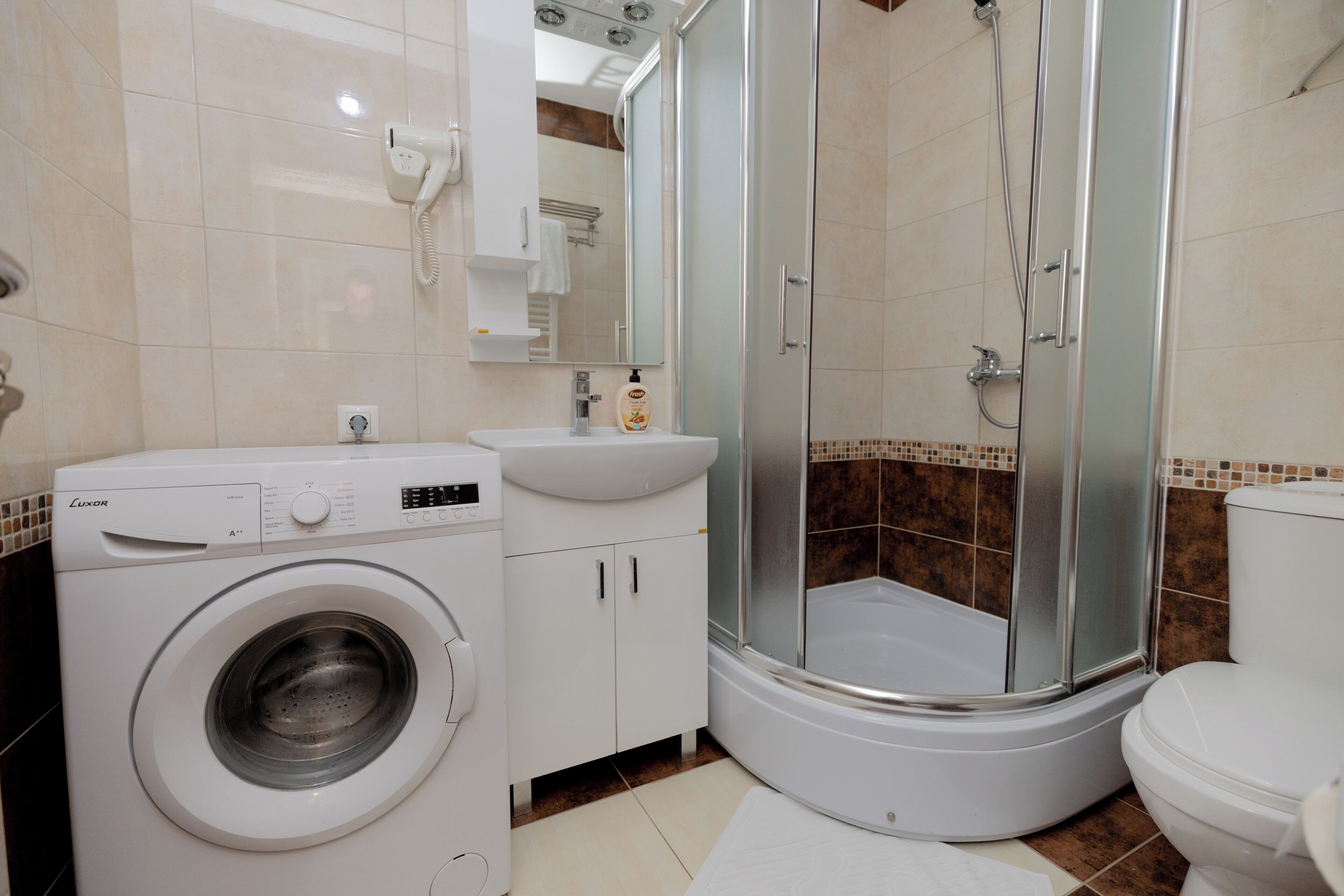 A modern bathroom with a washing machine, a sink, and a glass-enclosed shower.