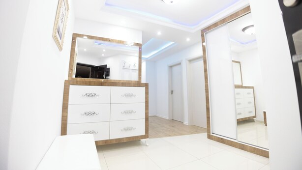 Un dormitorio moderno con un espejo grande, un armario con tiradores decorativos e iluminación empotrada en el techo.