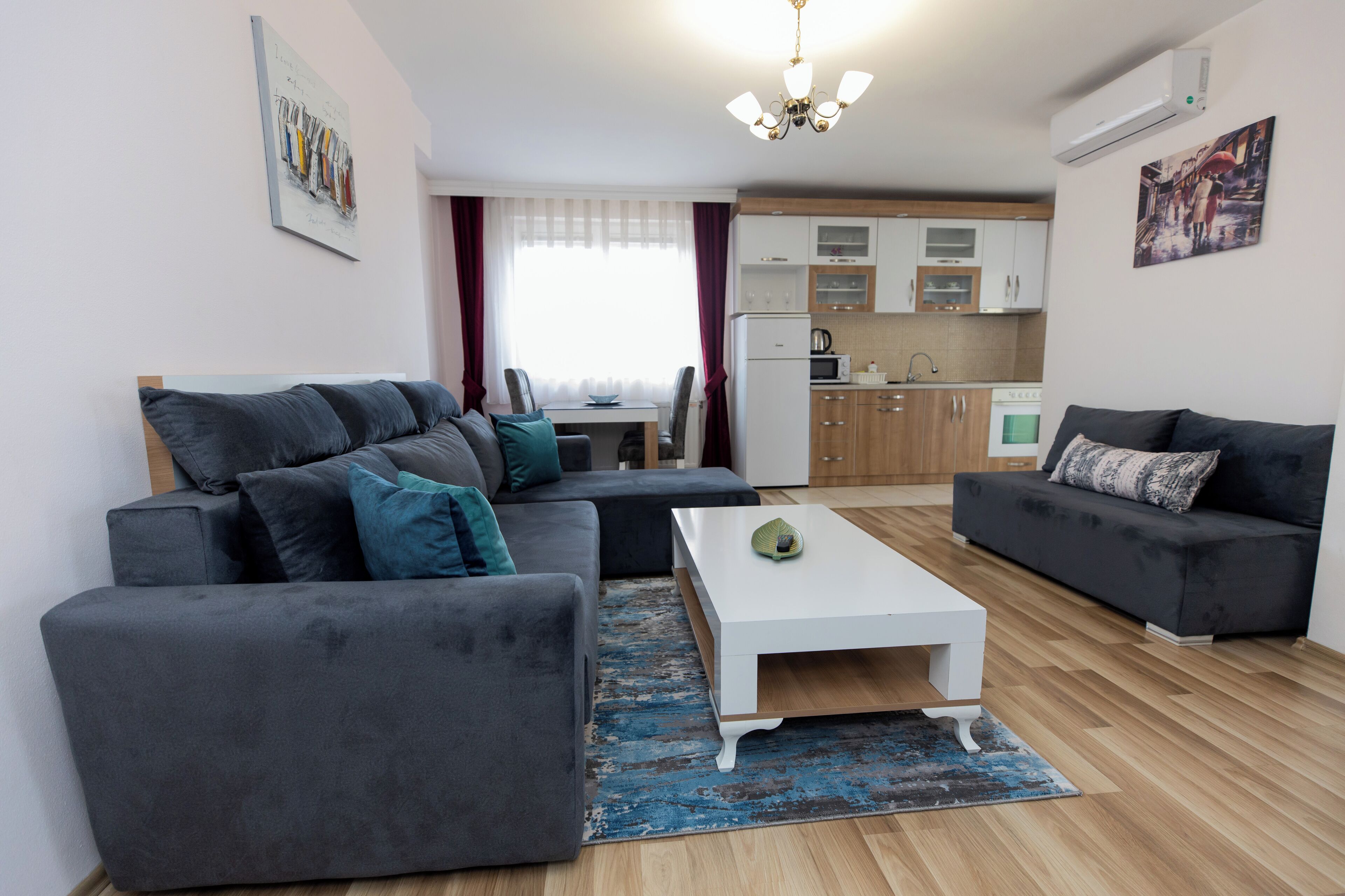 A modern living room with a grey sectional sofa, a white coffee table, and a grey sofa. The room has wooden flooring and a blue rug.