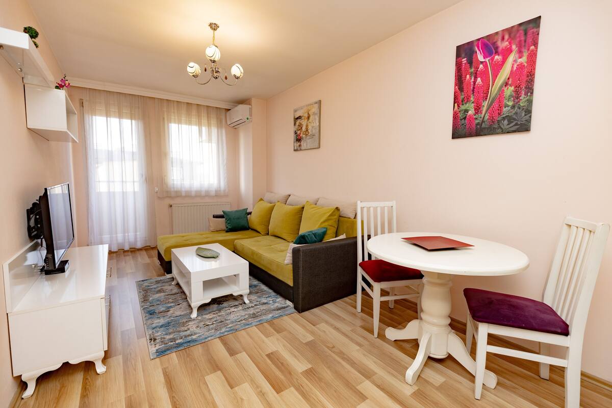 Ein modernes Wohnzimmer mit Sofa, Couchtisch, TV-Schrank und einem Essbereich mit Tisch und Stühlen.