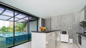 A modern kitchen with a glass-enclosed pool area, a microwave, and a coffee maker. - Designer Sea View Villa Natural Touch A1 (Kamala)