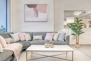 Ein modernes Wohnzimmer mit einem grauen Ecksofa, einem weißen Couchtisch und einem großen, abstrakten Gemälde an der Wand.