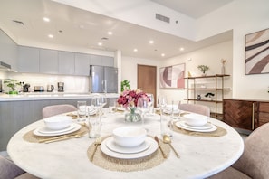 A modern kitchen with grey cabinets, a central island, and a dining area set for six with white plates, gold cutlery, and a vase of flowers.