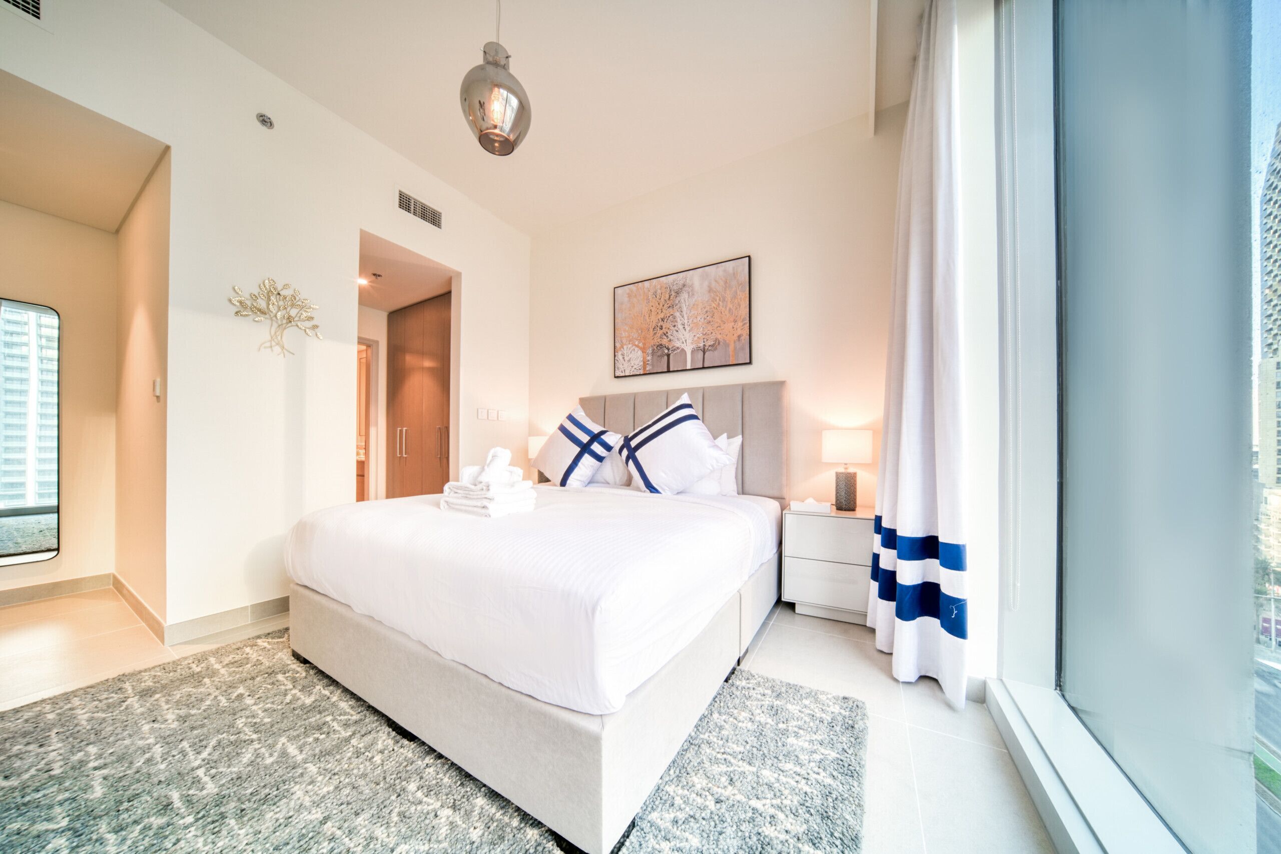 A hotel room with a bed, bedside table, lamp, and a view through the window.