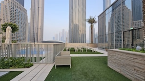 A rooftop garden with artificial grass, seating areas, and a view of surrounding high-rise buildings.