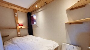 Een slaapkamer met een bed, een raam, een radiator en houten balken in het plafond.