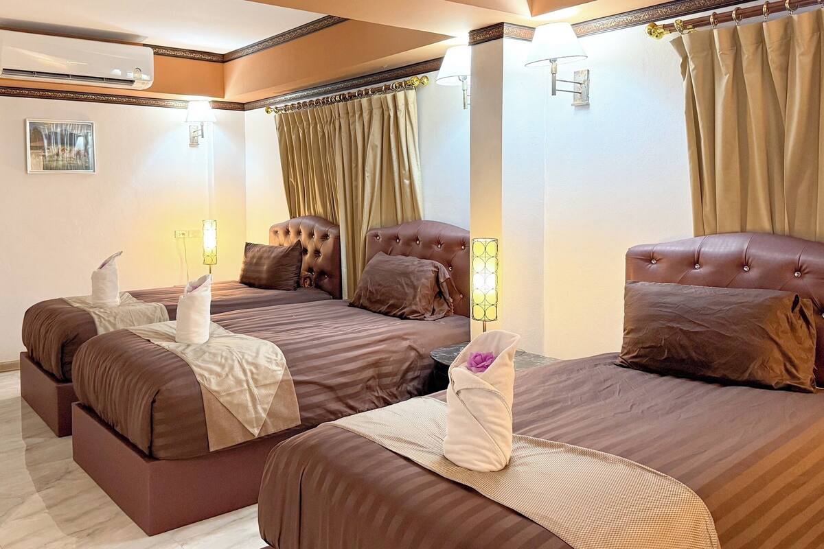 Ein Hotelzimmer mit zwei Betten, jedes mit einer gepolsterten Kopfteil und brauner Bettwäsche. Zwei Nachttischlampen, eine Wandklimaanlage und ein gerahmtes Bild sind ebenfalls vorhanden.
