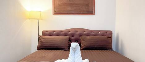 A neatly made bed with a brown headboard, a bedside lamp, and a framed picture on the wall.