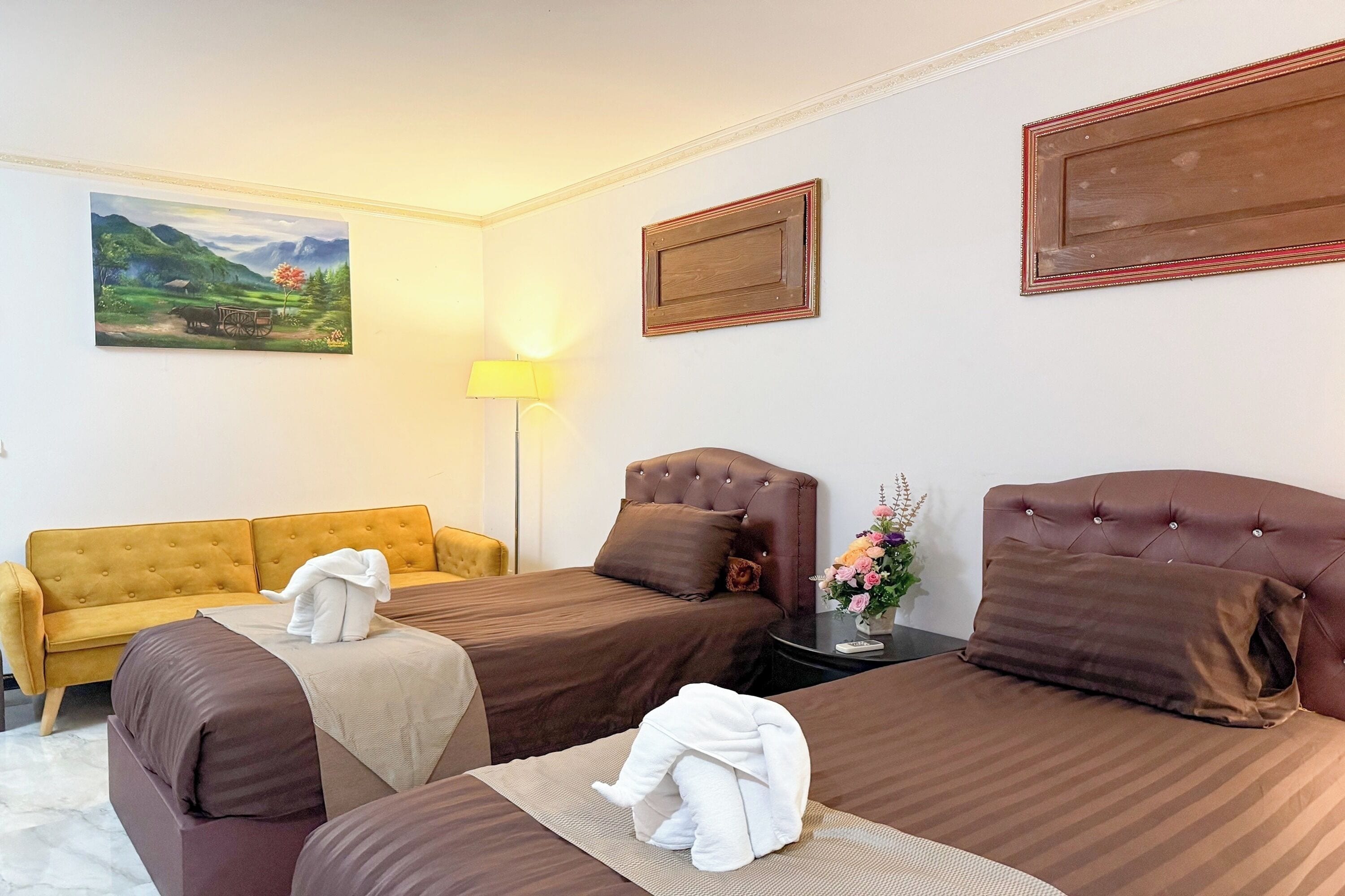Ein Hotelzimmer mit zwei Betten, einem Sofa, einer Lampe und einem Bild an der Wand.