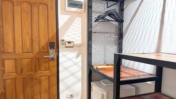 Una habitación con puerta de madera, pared blanca con termostato, ventana de malla metálica y radiador blanco.