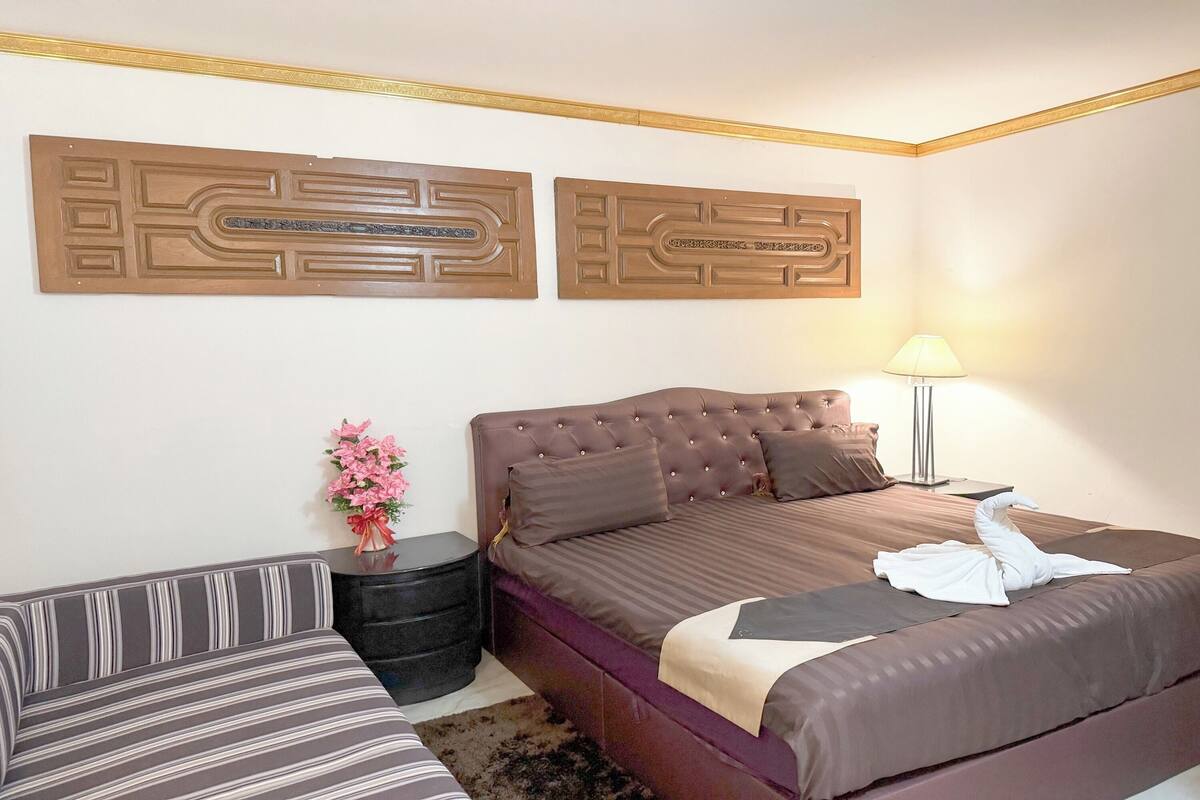 Ein Hotelzimmer mit einem großen Bett, einer Couch, einem kleinen Tisch mit Blumenvase und zwei dekorativen Wandpaneelen.