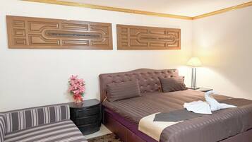 Habitación de hotel con una cama grande, un sofá, una mesita con un jarrón de flores y dos paneles decorativos en la pared.