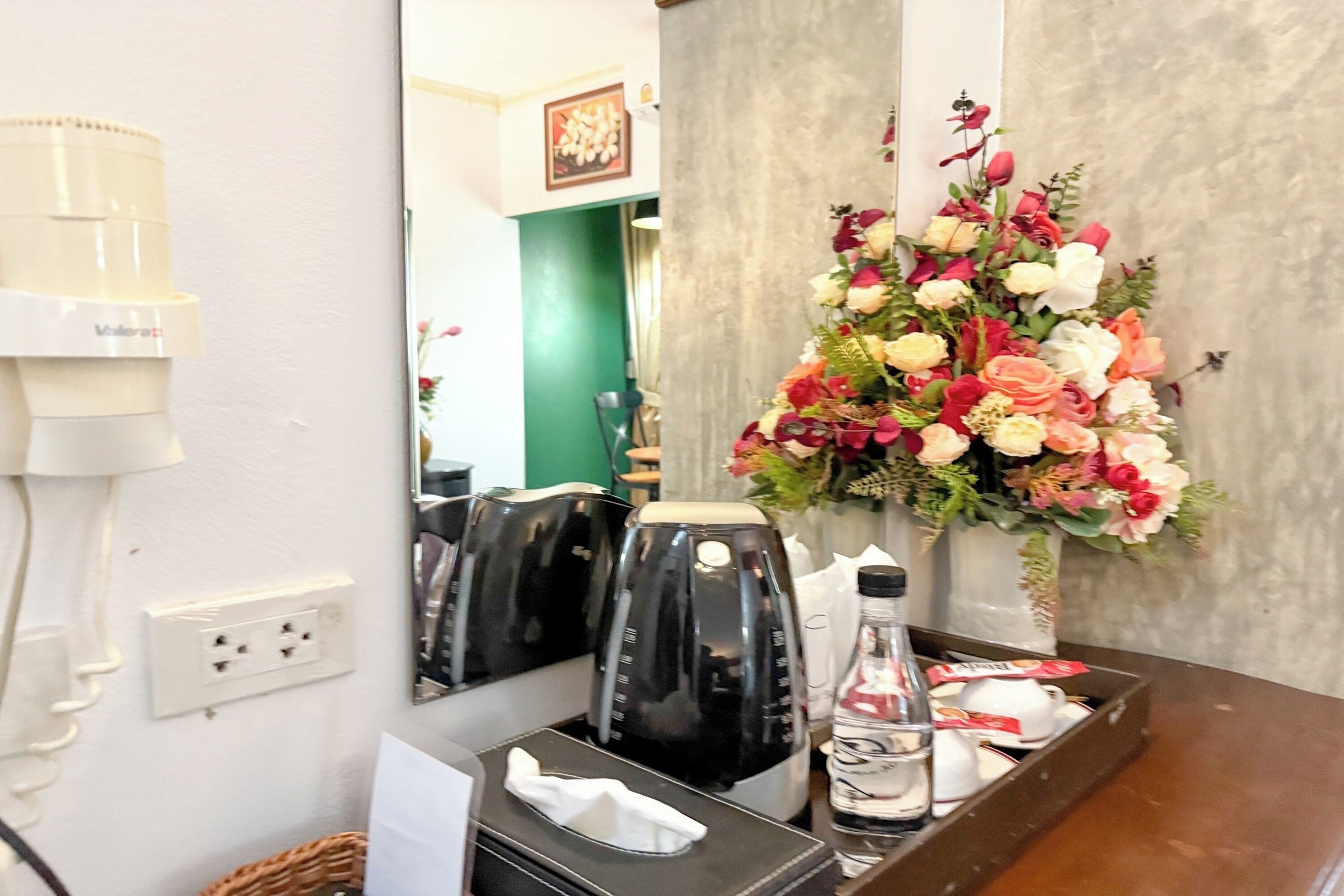 Ett hotellrum med en kaffebryggare, en vas med blommor, en flaska vatten och ett bricka med en näsdukask och en kopp.