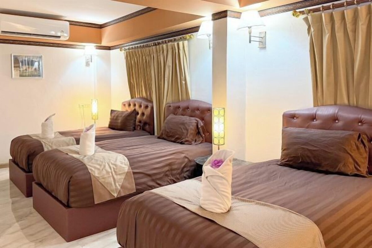 Quarto de hotel com duas camas, cada uma com travesseiro e toalha. Há um ar condicionado fixado na parede e uma mesinha com abajur.