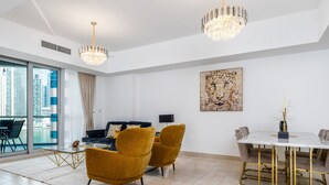A modern living room with a glass coffee table, mustard-colored chairs, a white sofa, a dining table with gold legs, and a chandelier. - Maison Privee - Sleek Apt with Dubai Marina Vws & Premium Facilities. (Dubai)