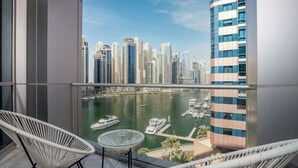 A balcony with two white wicker chairs and a small table, overlooking a marina with boats and tall buildings in the background. - Maison Privee - Sleek Apt with Dubai Marina Vws & Premium Facilities. (Dubai)