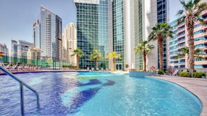 A swimming pool with a curved edge, surrounded by palm trees and modern buildings in the background. - Maison Privee - Sleek Apt with Dubai Marina Vws & Premium Facilities. (Dubai)
